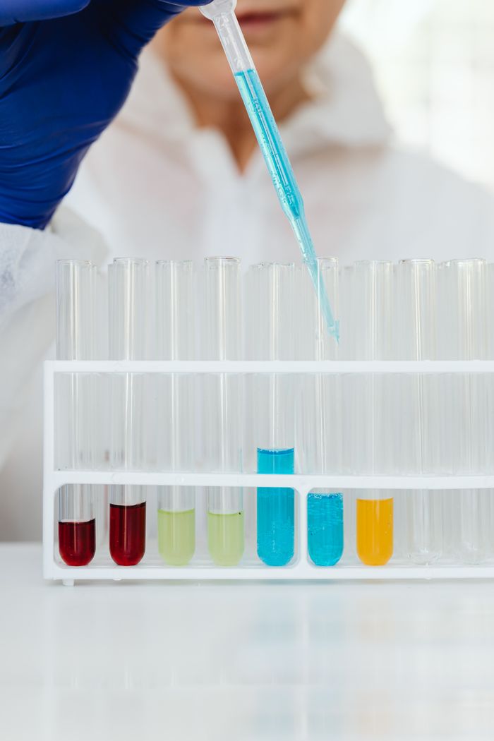 Scientist in protective gear using a pipette with colorful liquids in test tubes.